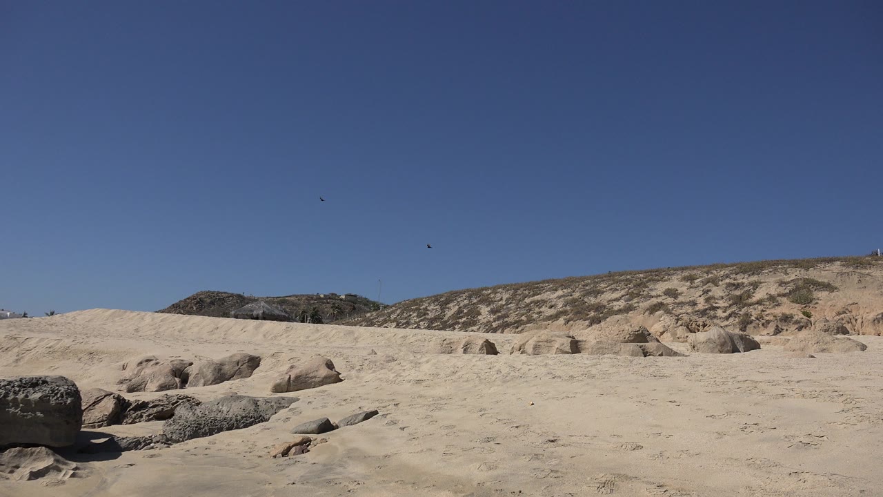Sandy terrain with scattered rocks, low hills, and clear blue sky.