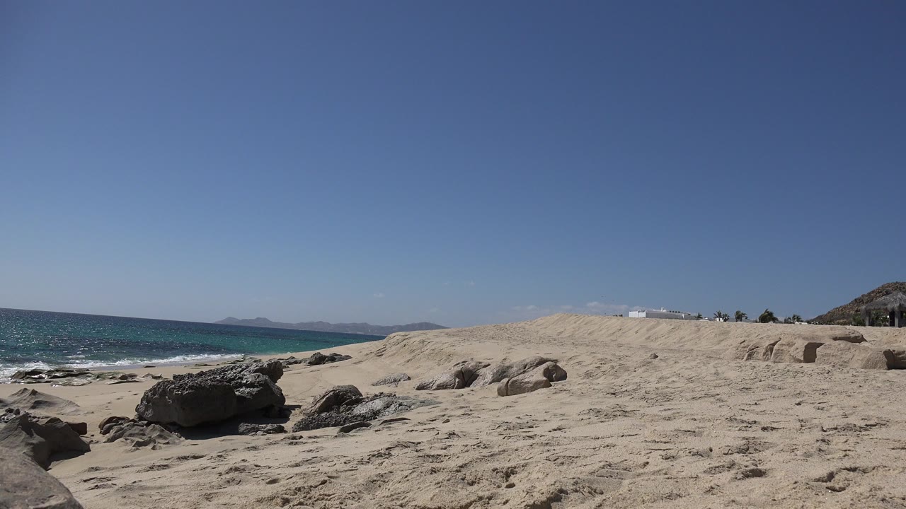 Sandy beach with rocks, blue ocean, and clear sky