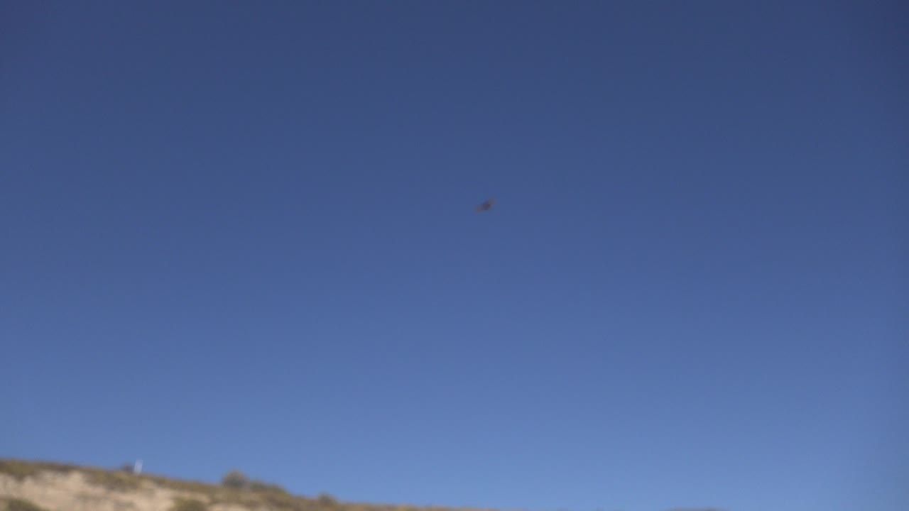 At 0:01, the flying object sits near the upper part of the Los Cabos sky while a narrow dry hillside runs along the bottom, with no visible people.