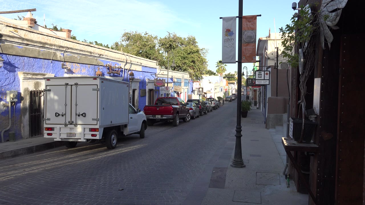 Narrow town road with a white box truck parked beside a blue building.