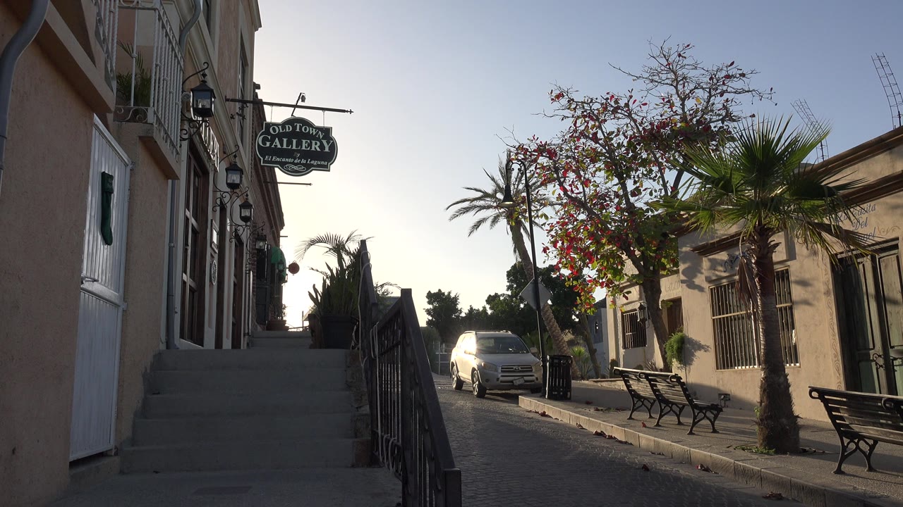 Sidewalk stairs beside a narrow street with a gallery sign and parked white car.