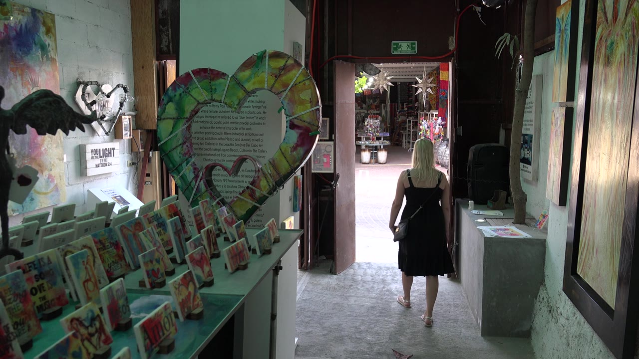 Art hallway with display racks and a person walking toward an open doorway.