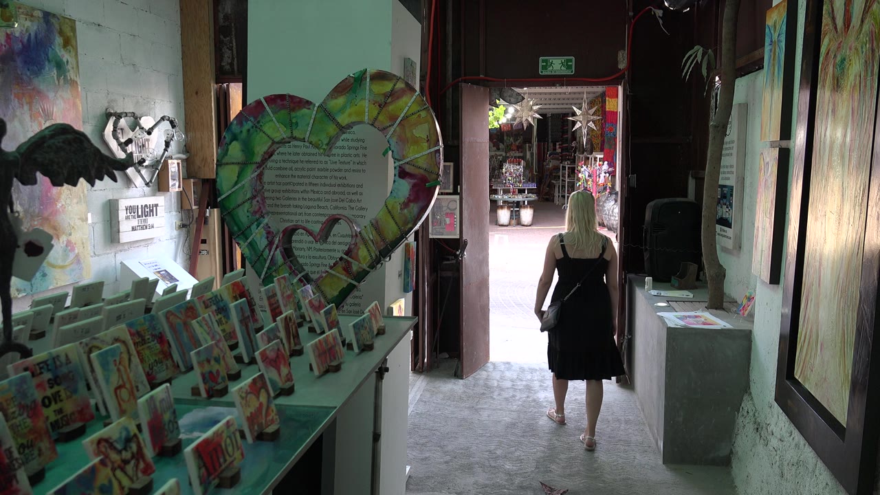 In the Los Cabos hallway, the visitor is farther along the walkway, framed by small colorful cards on the left and tall wall art on the right.