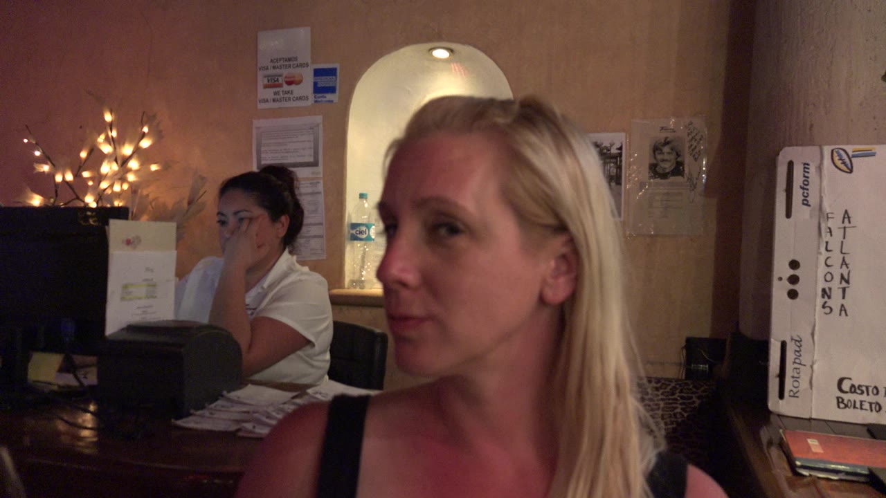 The woman turns slightly to the side in the Los Cabos restaurant, with warm decorative lights and posted wall signs visible behind her.