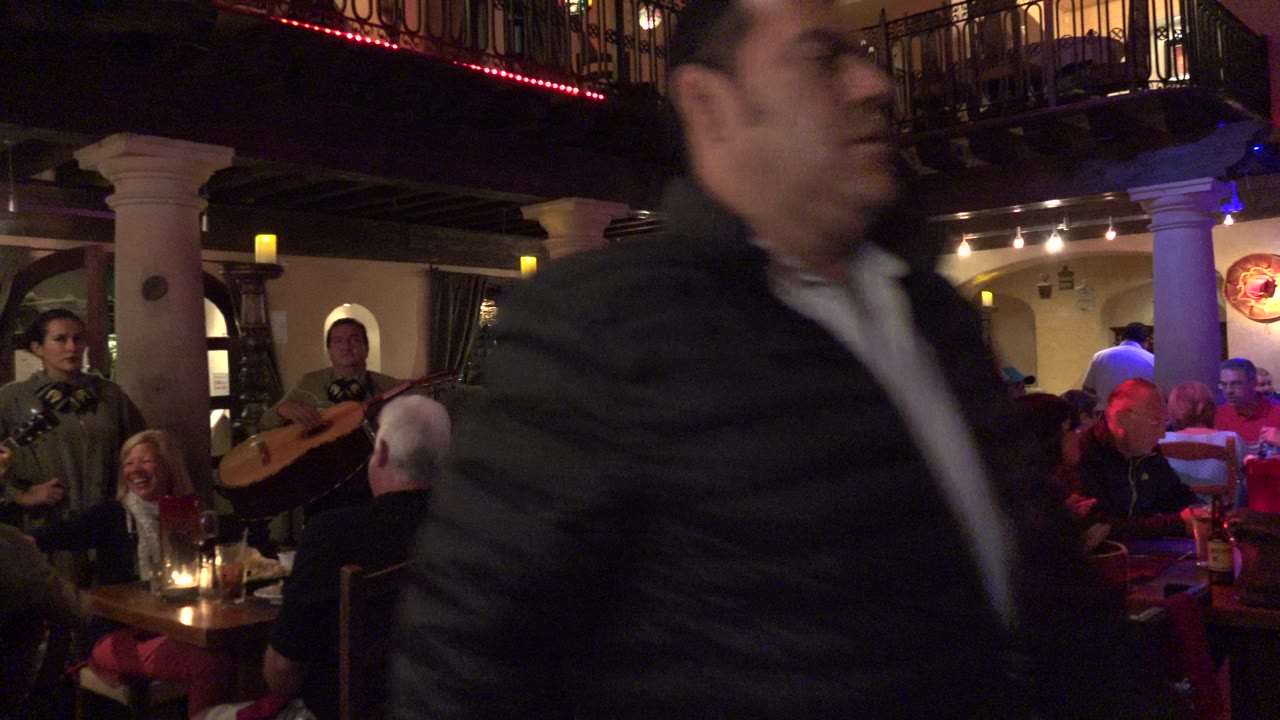 Blurred man passing in front of diners and mariachi musicians