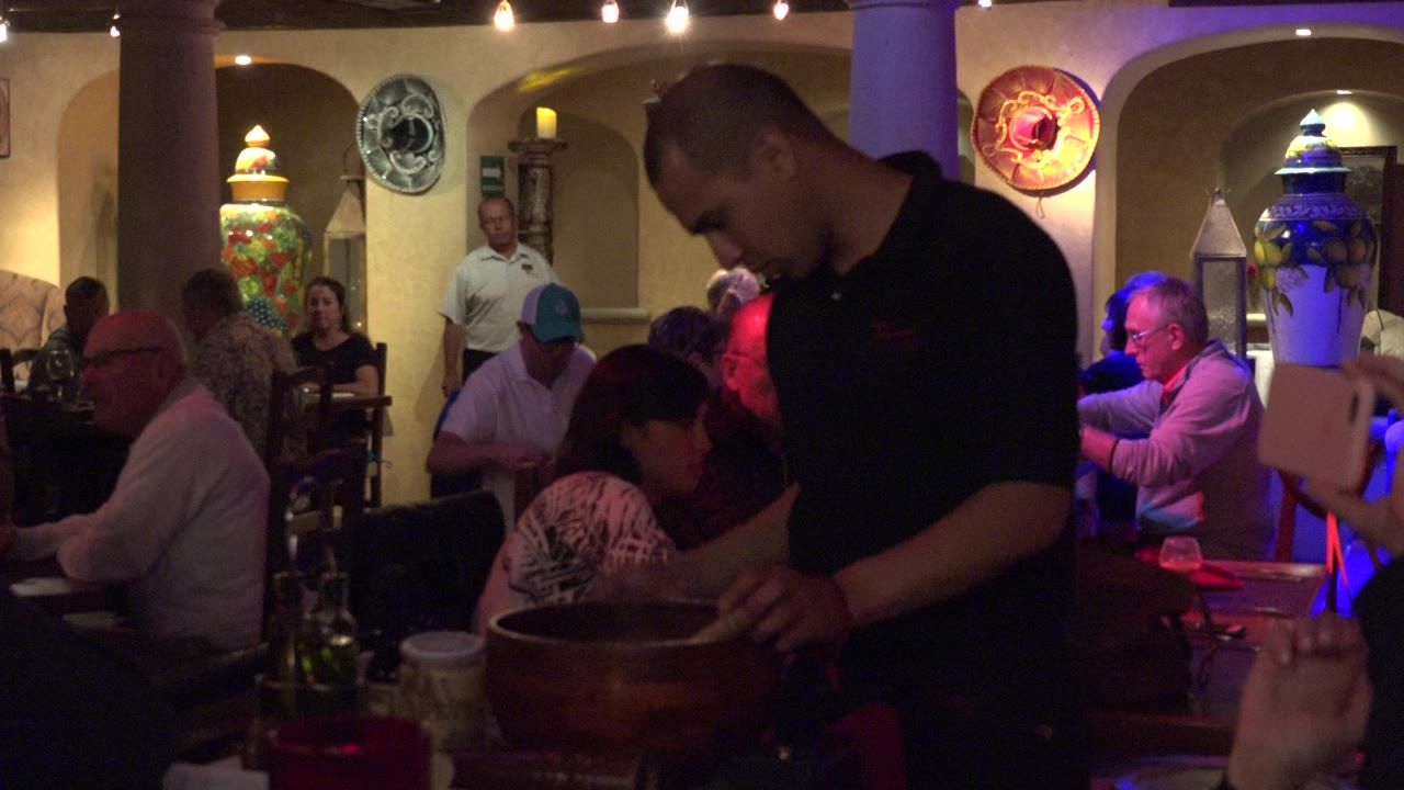 Server beside a wooden bowl in a busy restaurant dining room.