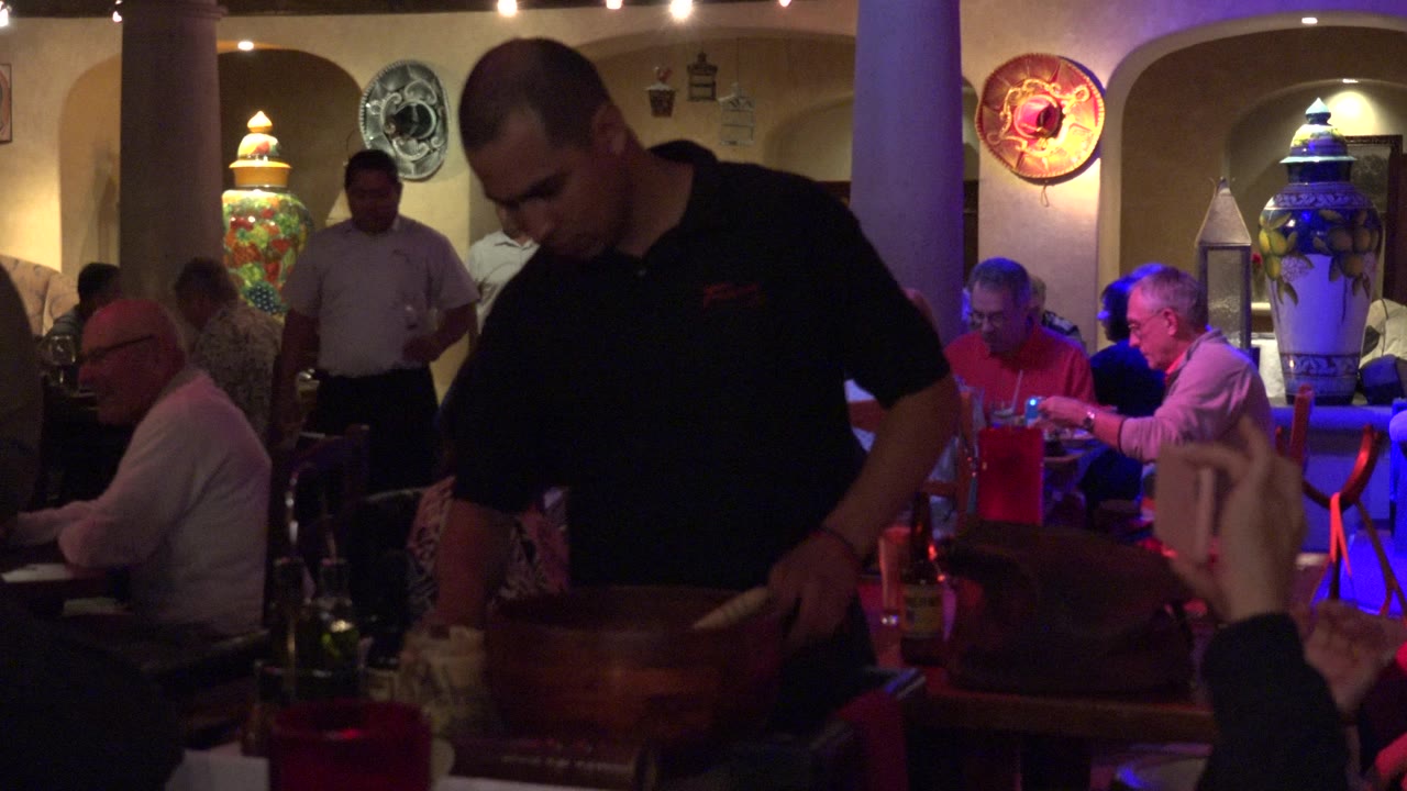 Restaurant staff member working beside a wooden bowl with diners behind him.