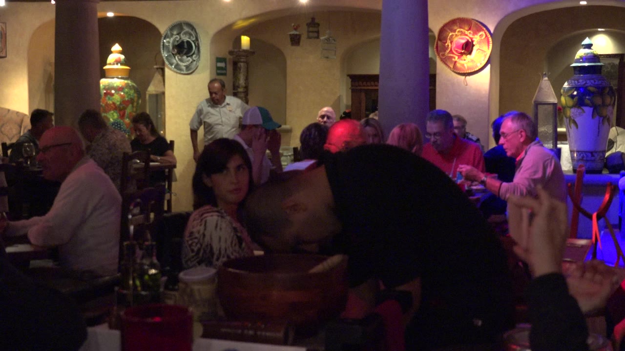 Los Cabos dining room view with patrons at several tables, a woman facing camera near the foreground, and colored red and blue light across the right side of the room.
