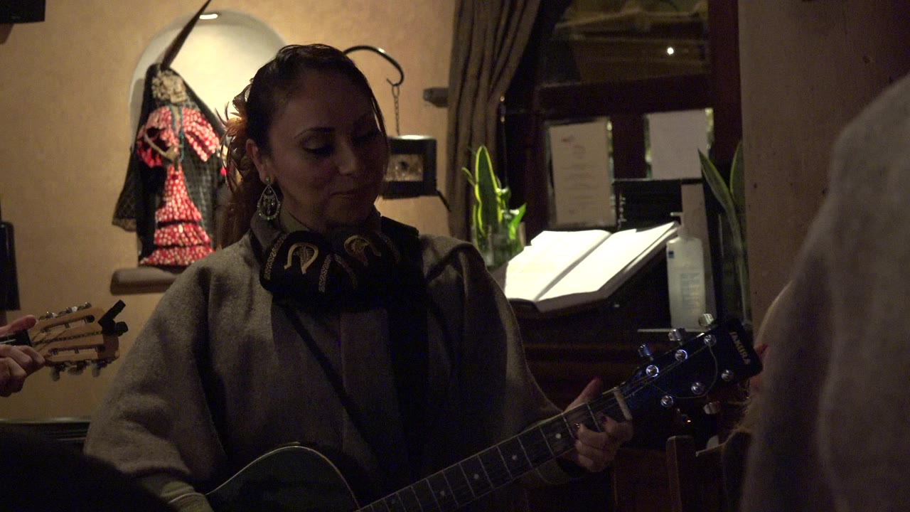 Woman playing guitar indoors with audience close to the camera.