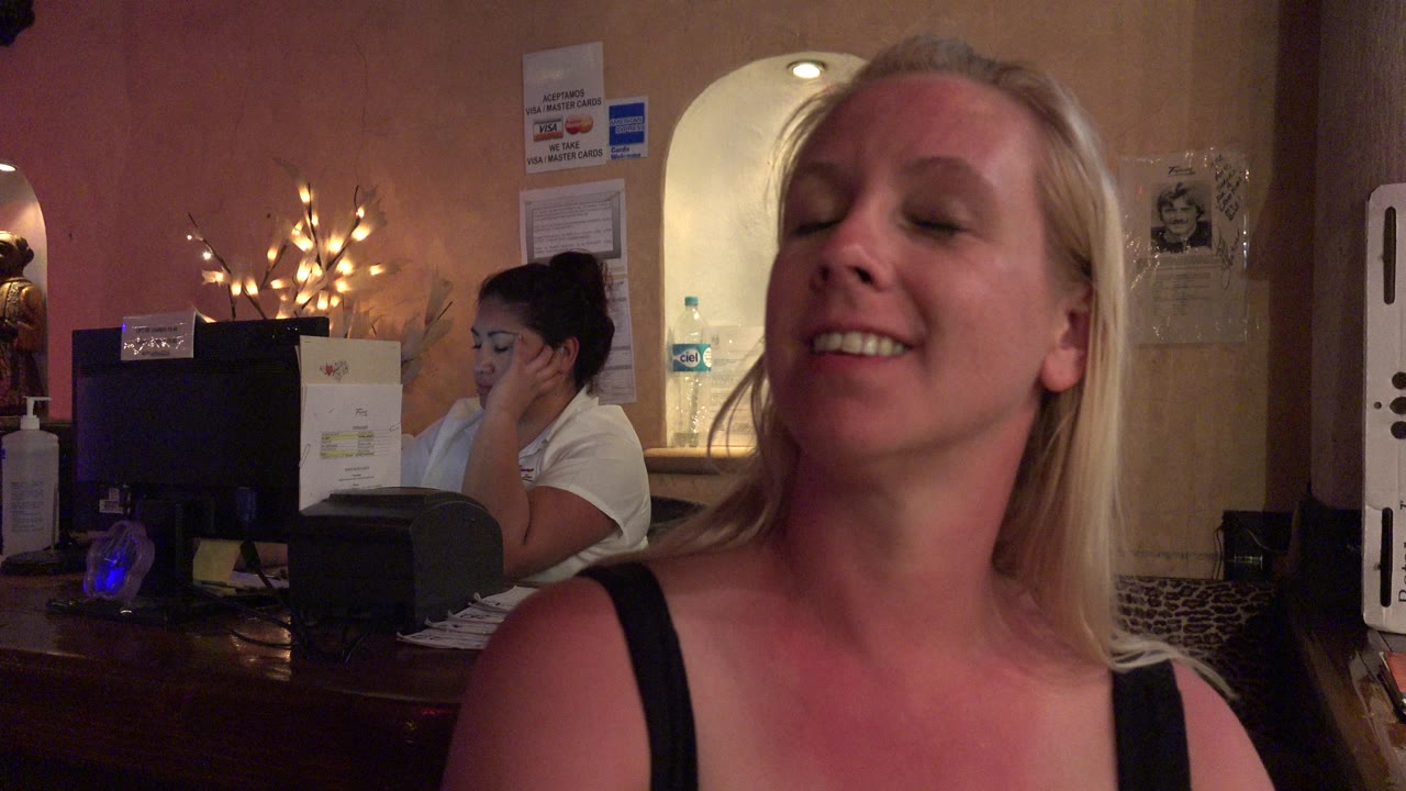 Blonde woman smiling near a reception desk indoors.