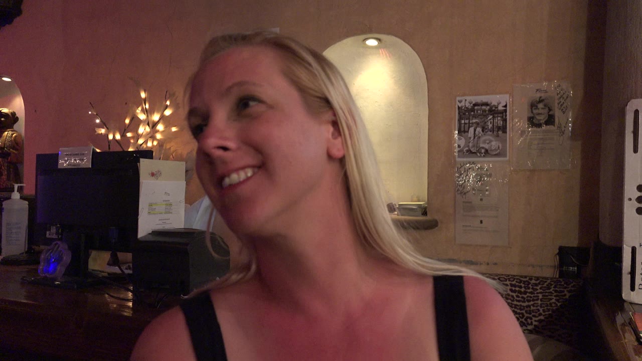 Blonde woman smiling in a dim restaurant interior.