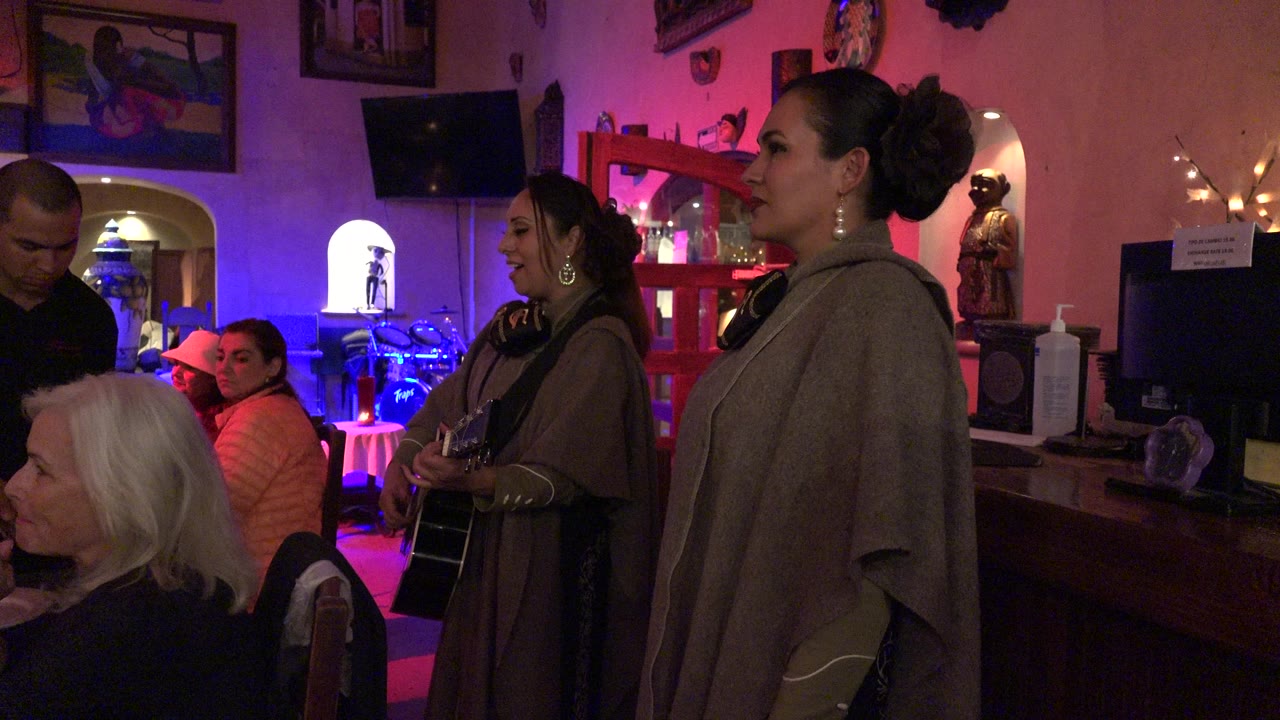 Women singing near seated diners in a dim restaurant interior