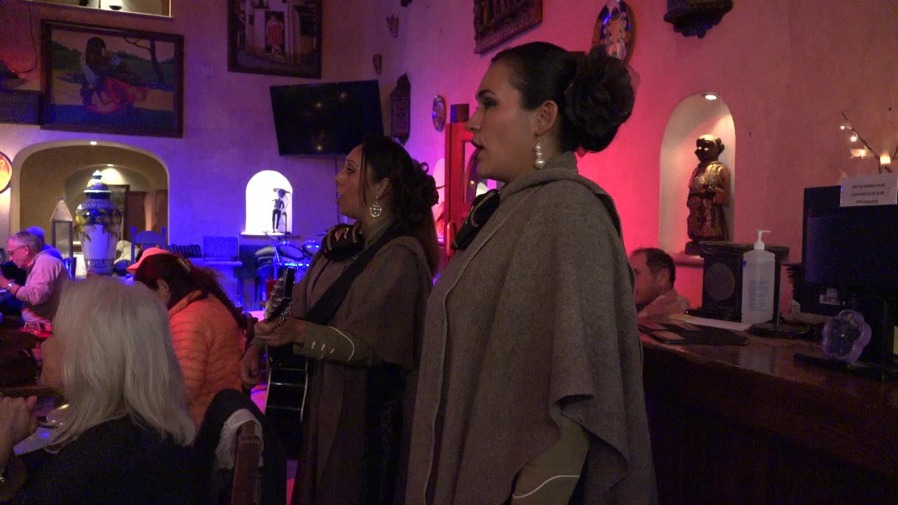 Two women performing near seated guests in a colorful indoor party room.