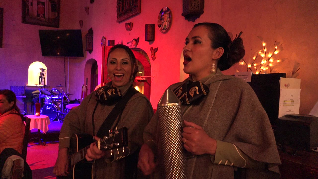 Two women singing with guitar and metal percussion instrument indoors