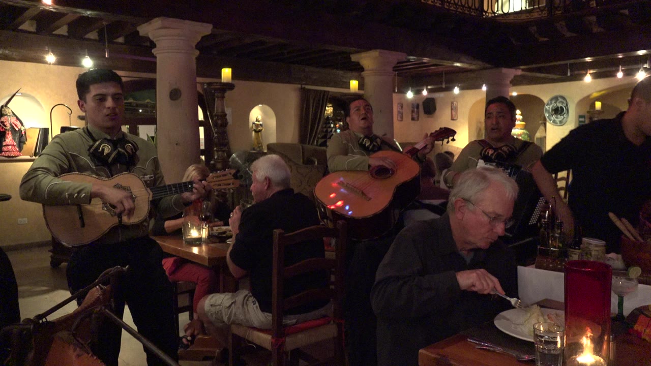 Musicians perform beside diners in a warm restaurant interior.