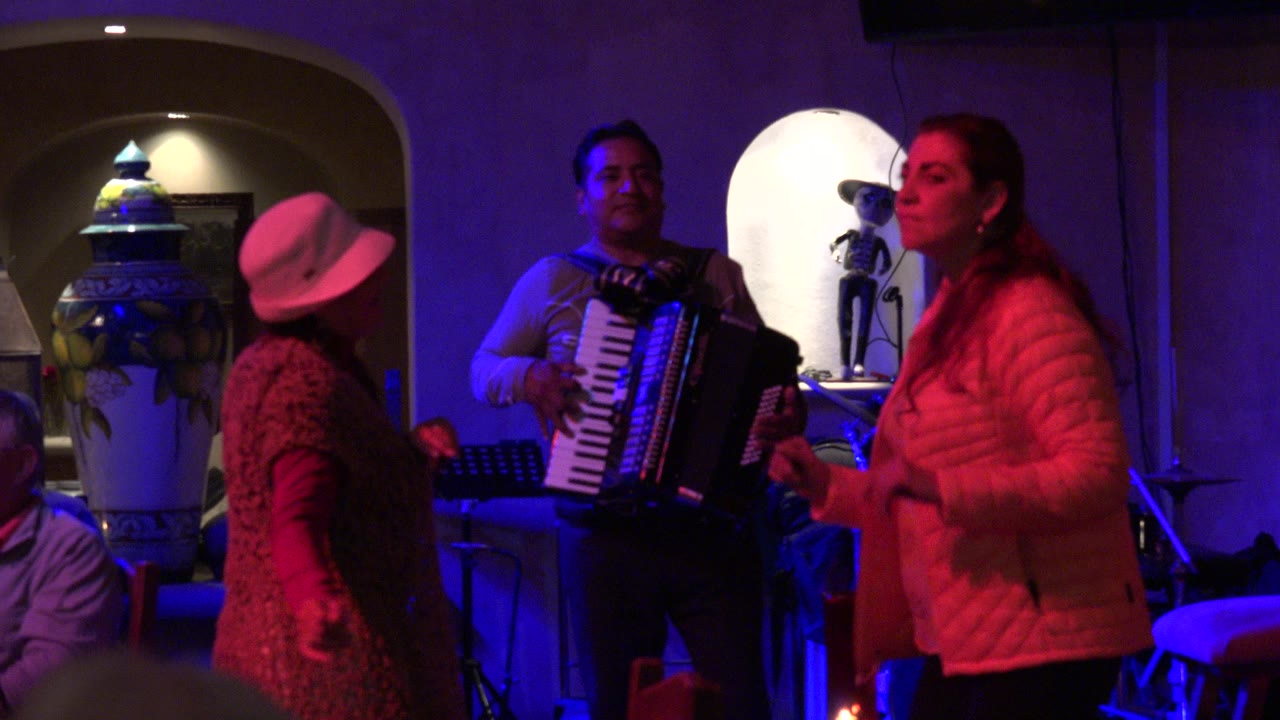 Two women dance near an accordion player under red and blue lighting.