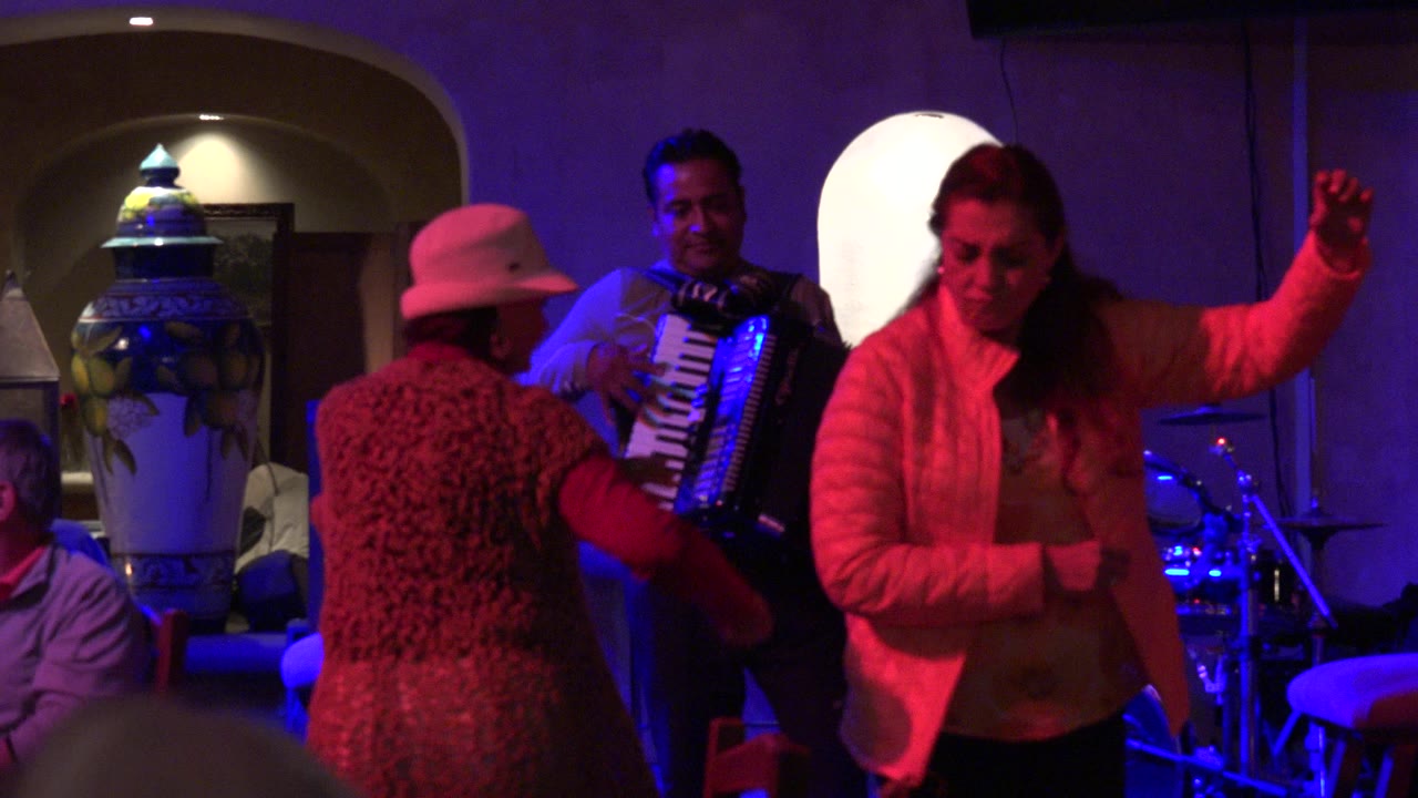 Two women dance in front of an accordion player under red and blue lights.