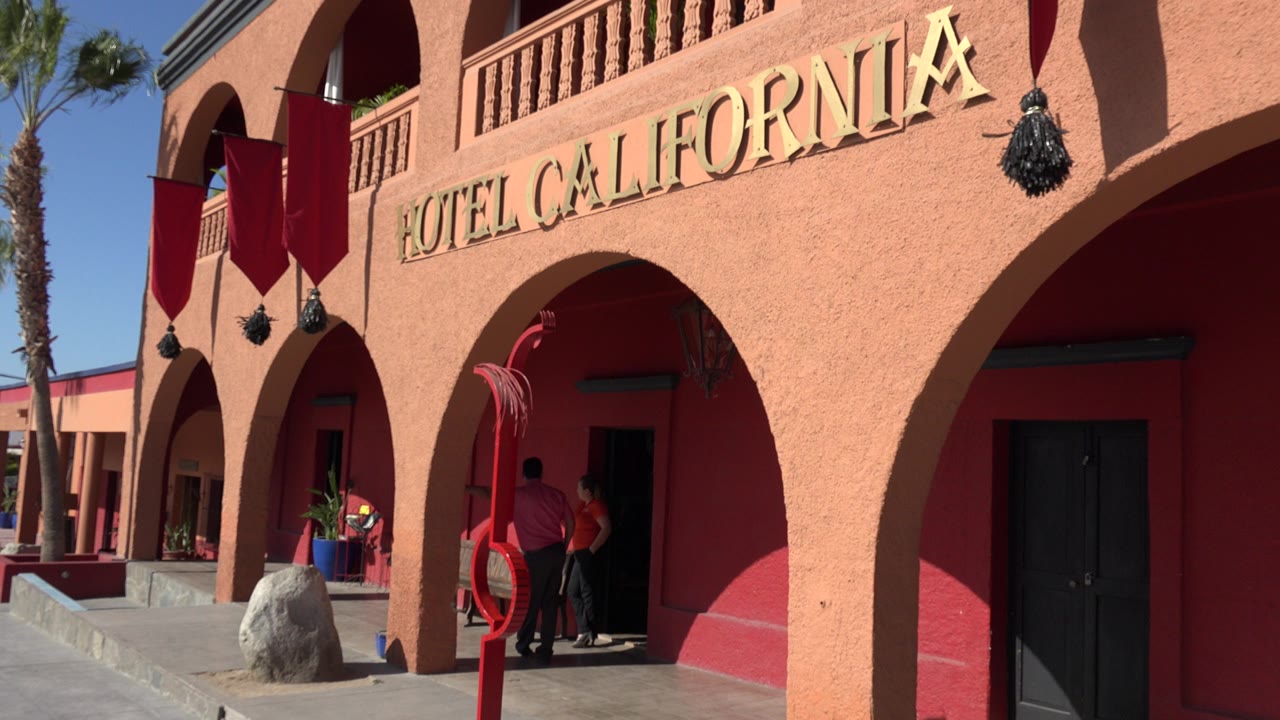 At 0:00, a Los Cabos hotel exterior shows gold Hotel California lettering above peach arches, red banners, and visitors standing near a shaded doorway.