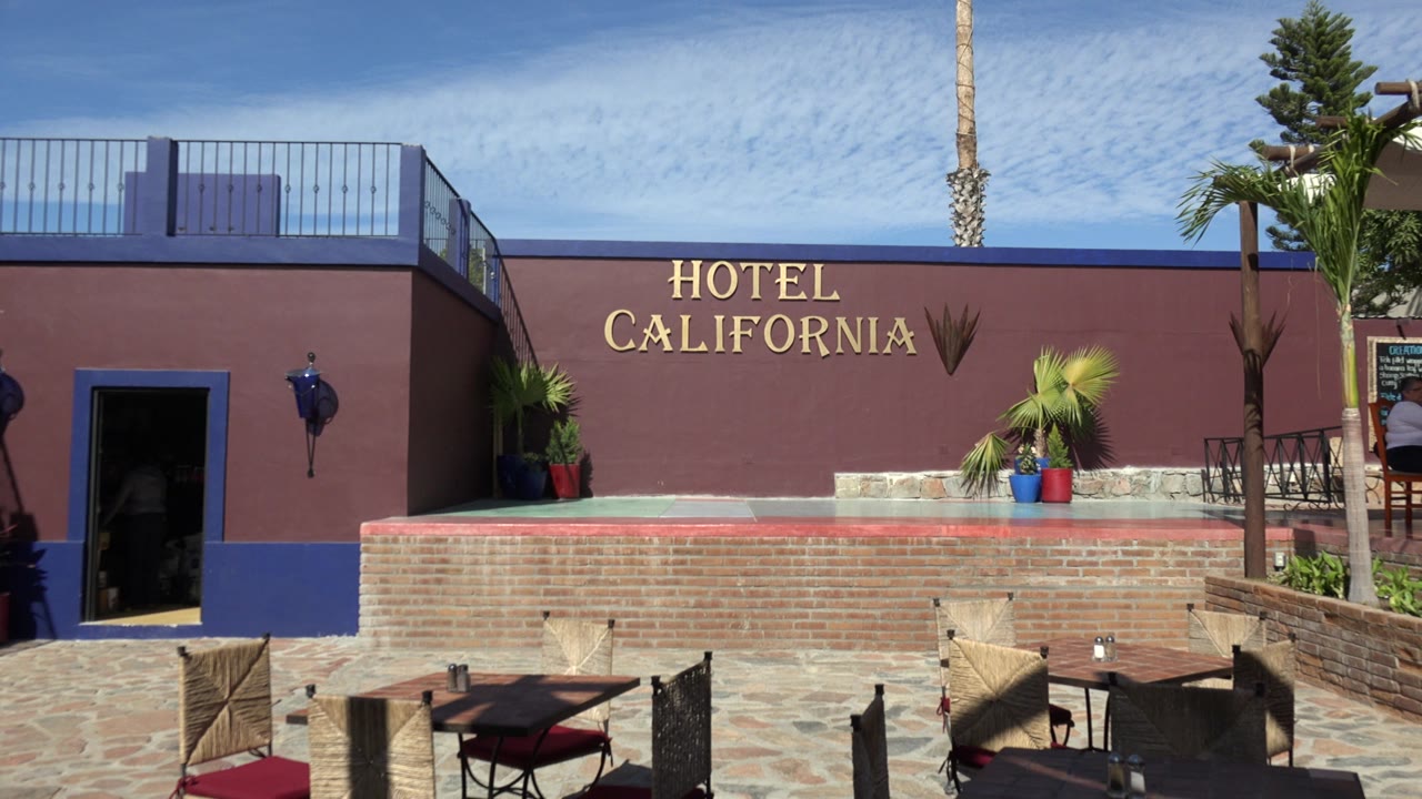 Hotel California sign on a brown building above patio seating.