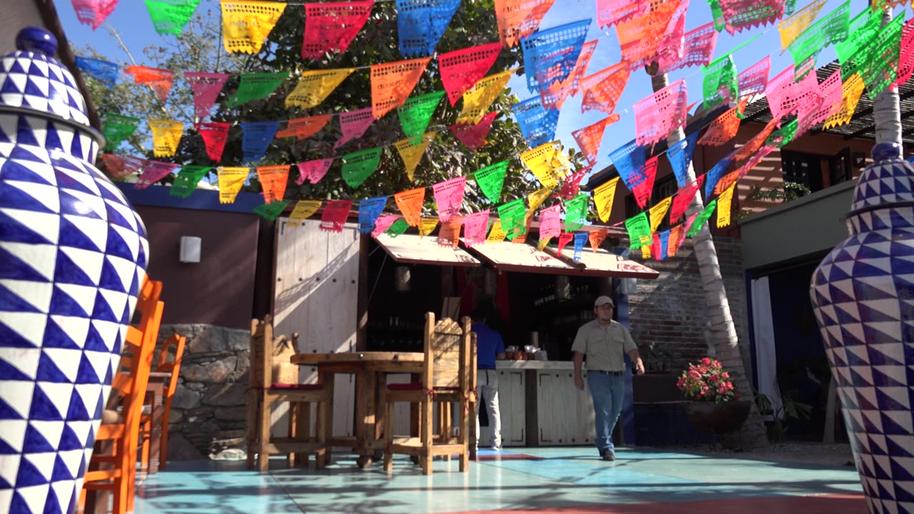Colorful flags over a patio with large blue-and-white vases and a man in the distance.