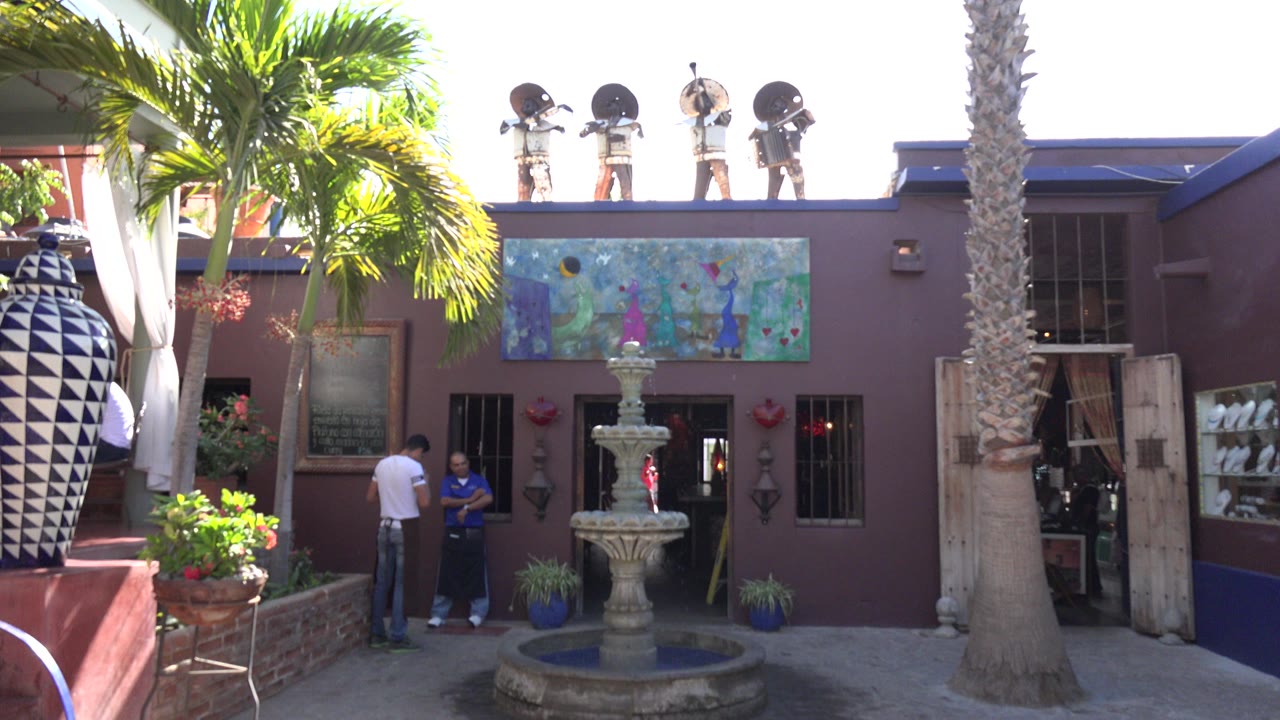 Resort building facade with fountain, palms, and two people near the entrance.