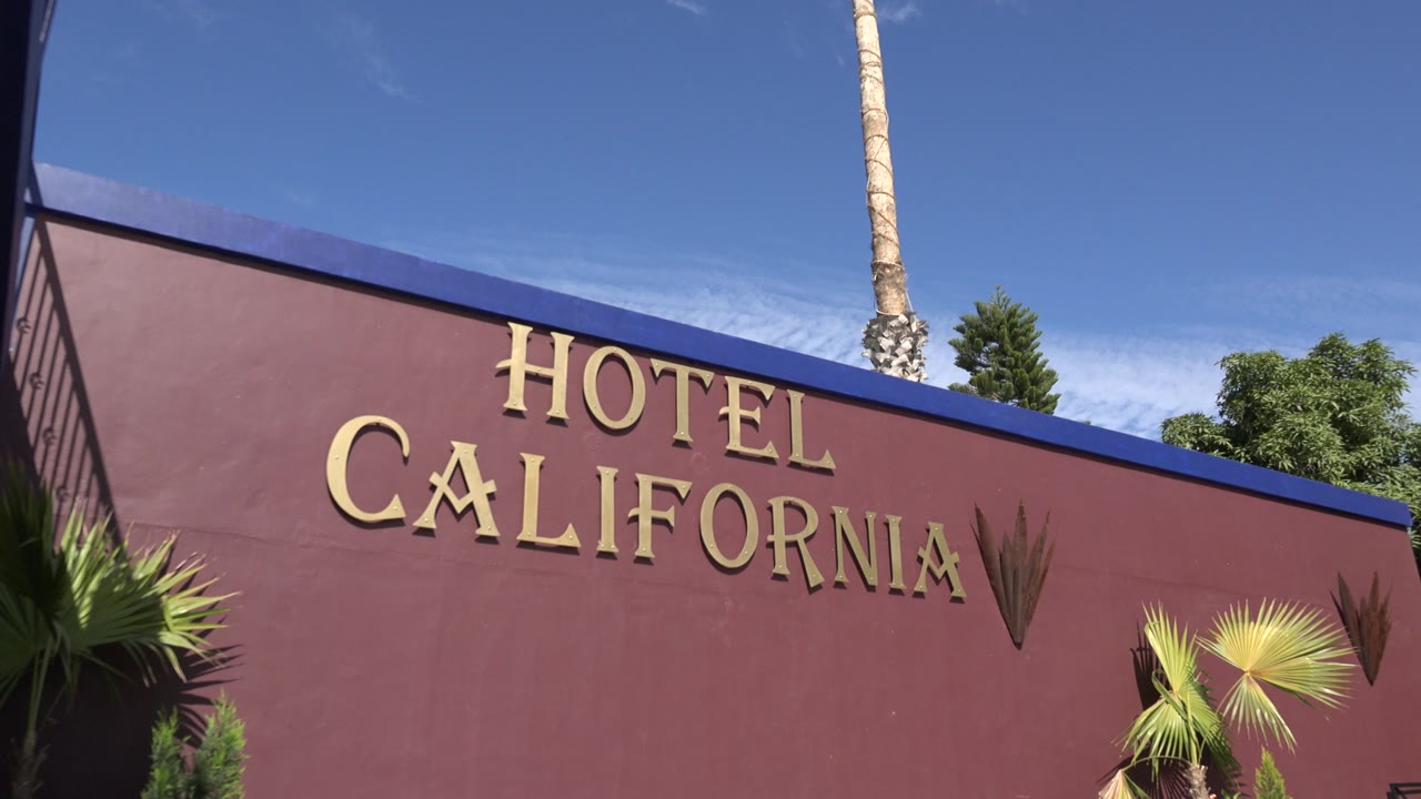 Hotel California sign on a burgundy wall below blue sky.