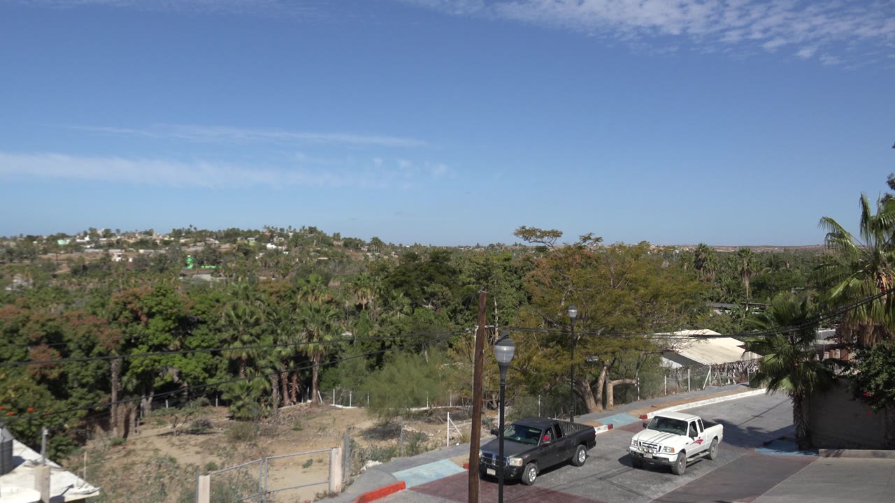 White pickup near the right side of a residential street with trees and hills behind.