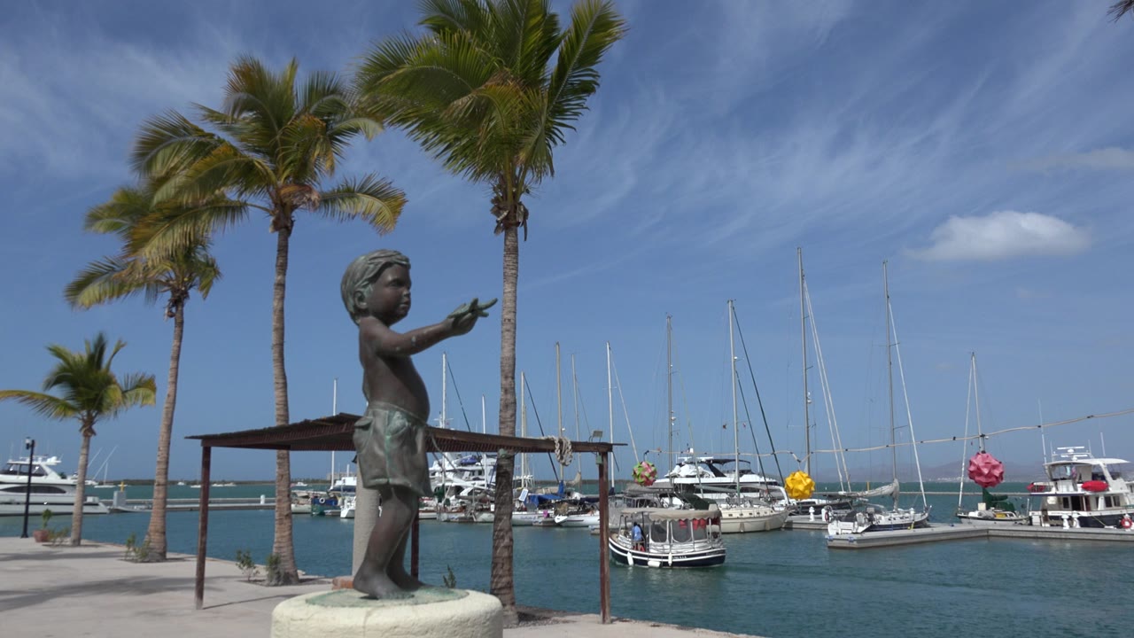 Marina boats behind a bronze statue and palm trees