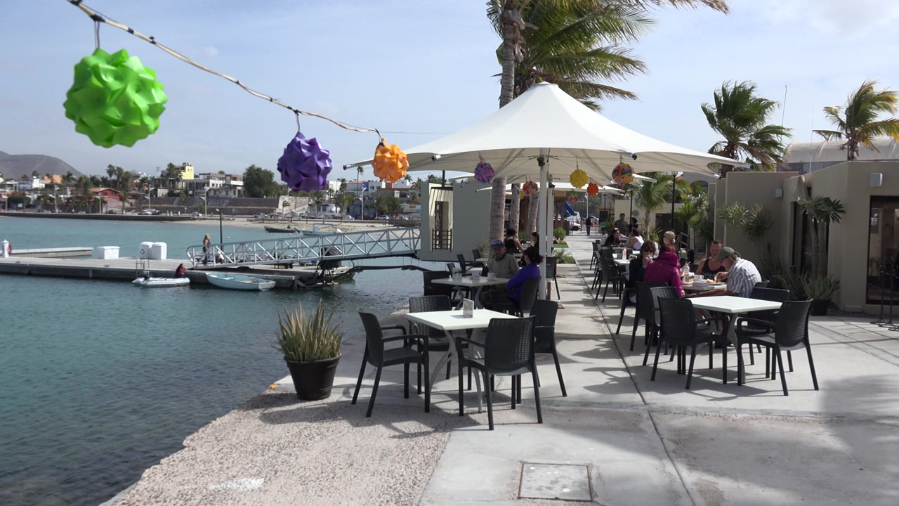 Outdoor restaurant patio beside marina water with colorful hanging decorations.