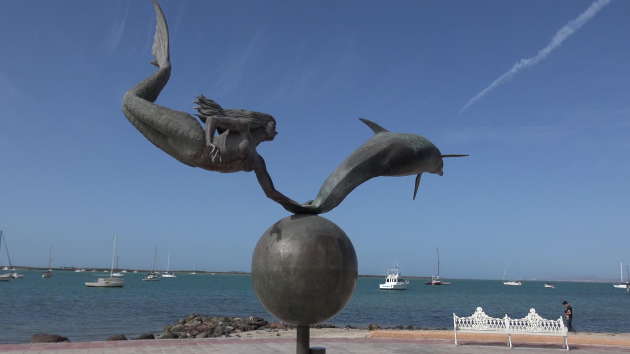 Large waterfront statue with boats and a white bench behind it