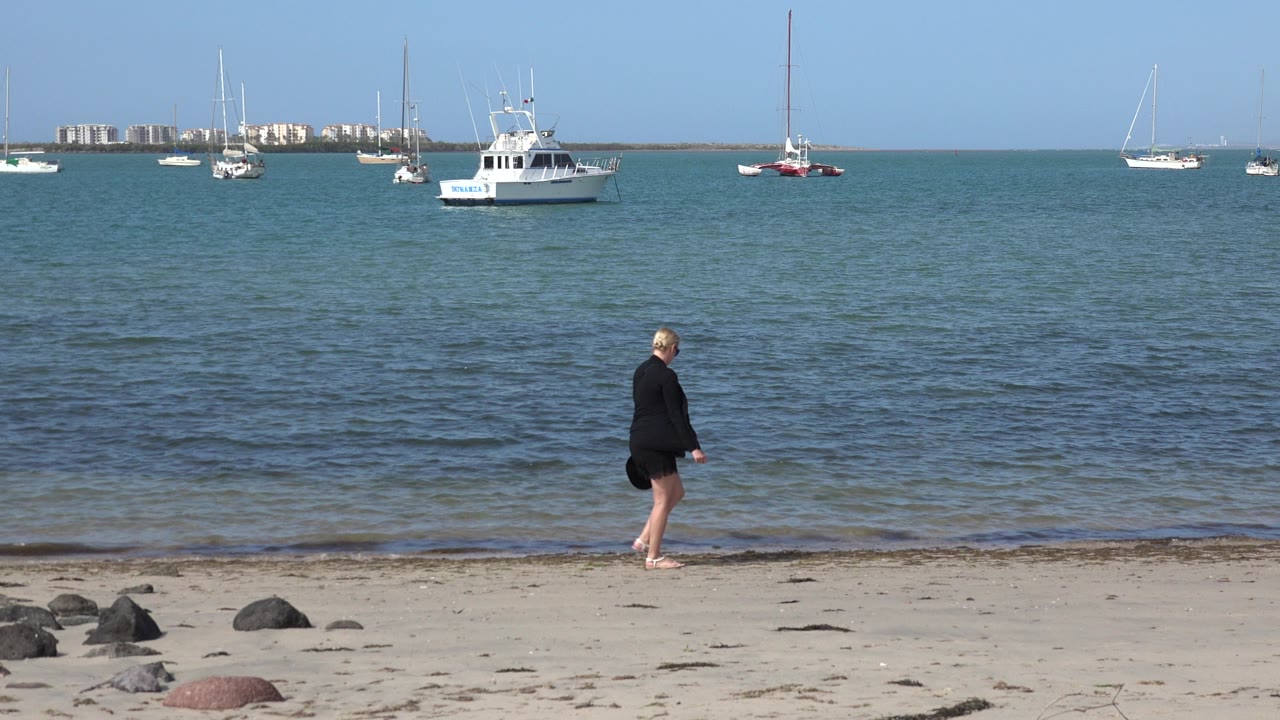 Woman walking along a sandy beach with boats offshore