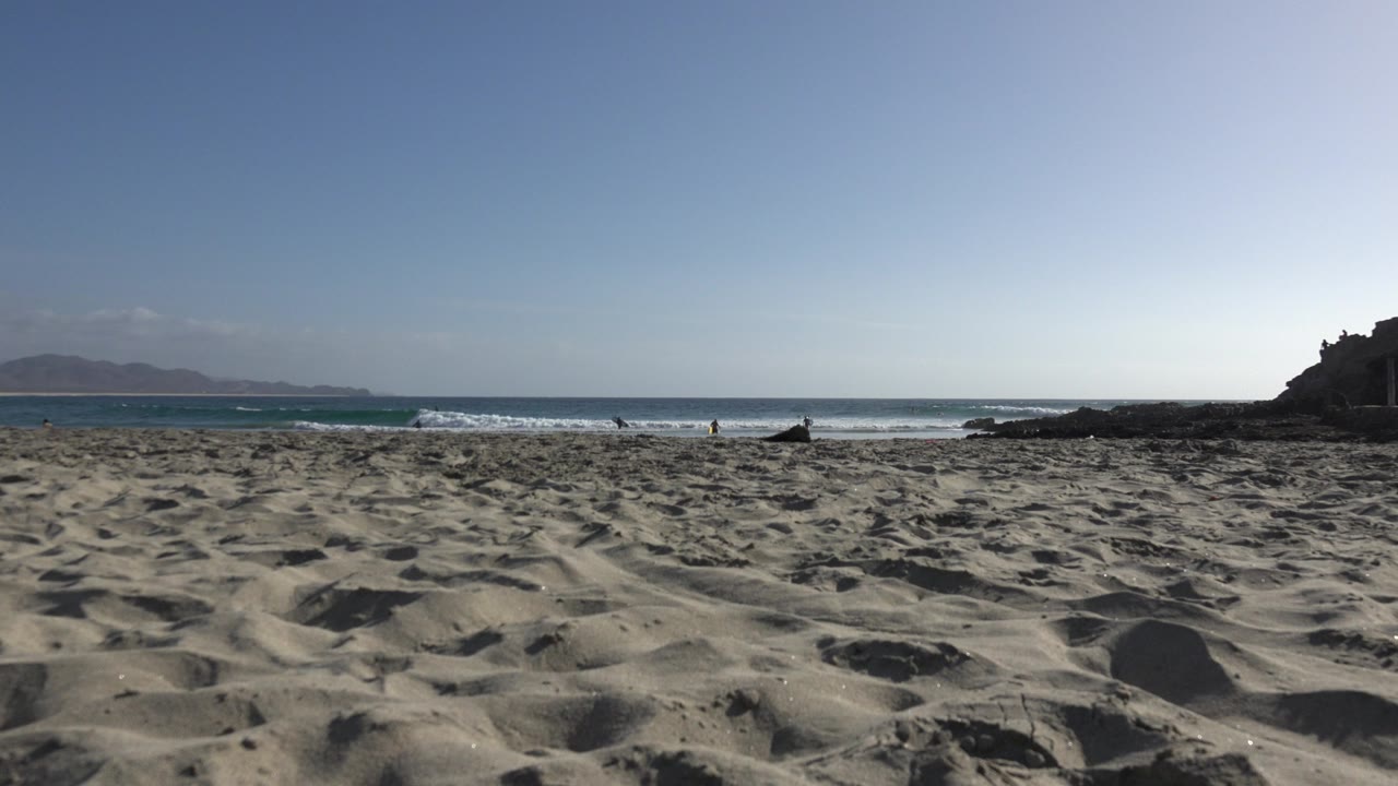 Sandy beach with ocean waves and a rocky point under blue sky.