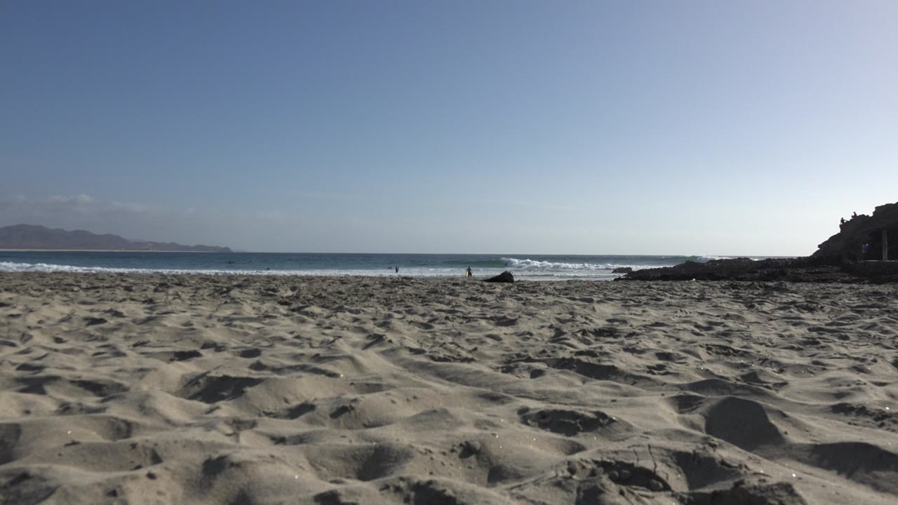 Low view of sandy beach with waves and a rocky point at right.