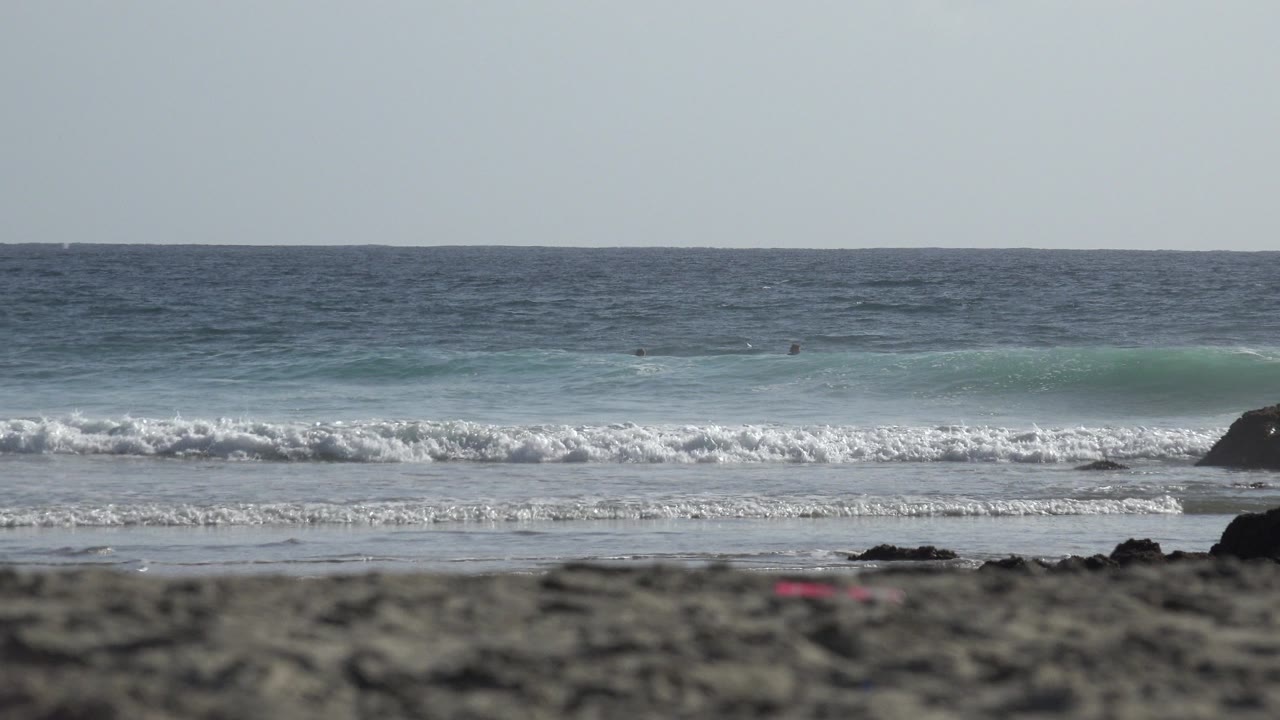 Ocean waves breaking near dark rocks beyond a sandy foreground.