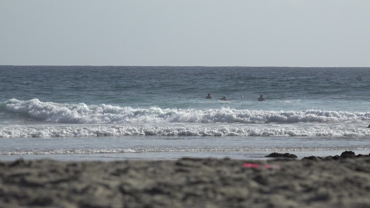Beach surf with blurred foreground sand and distant people in the water