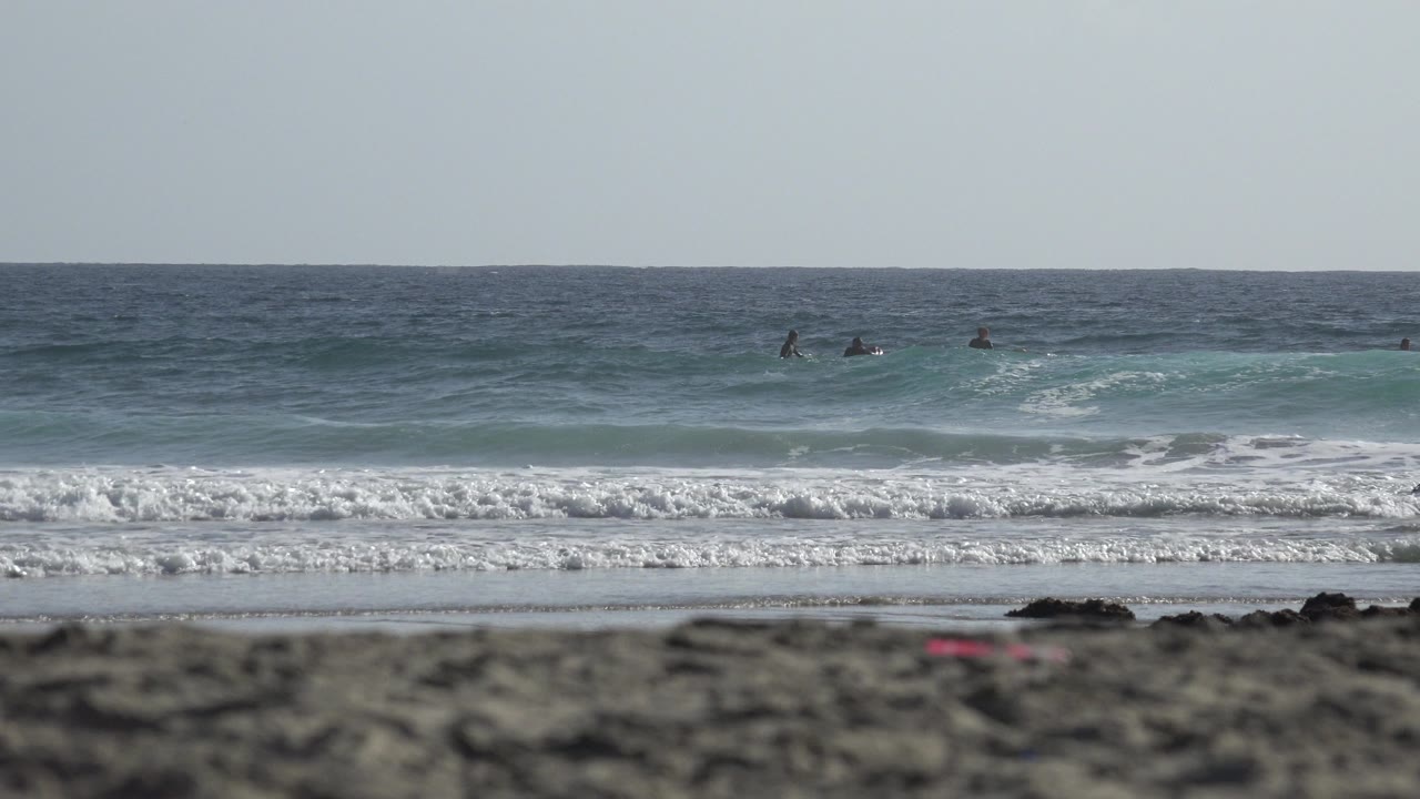 Low beach view with surf, horizon, and distant people in the water.