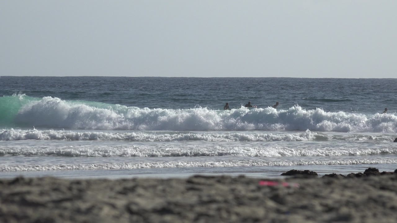 White surf breaking behind a blurred rocky beach foreground.