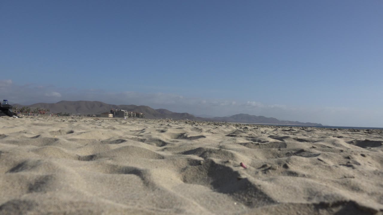Wide sandy foreground with distant mountains and ocean edge
