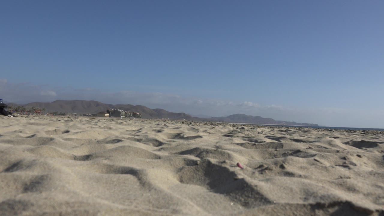 Wide sandy shoreline view with low horizon, mountains, and open sky.