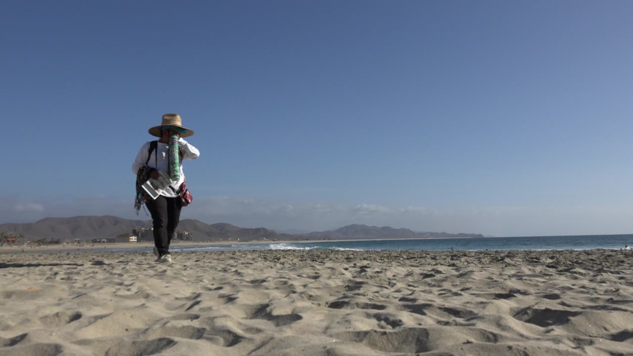 Beach vendor walking across sand with ocean behind
