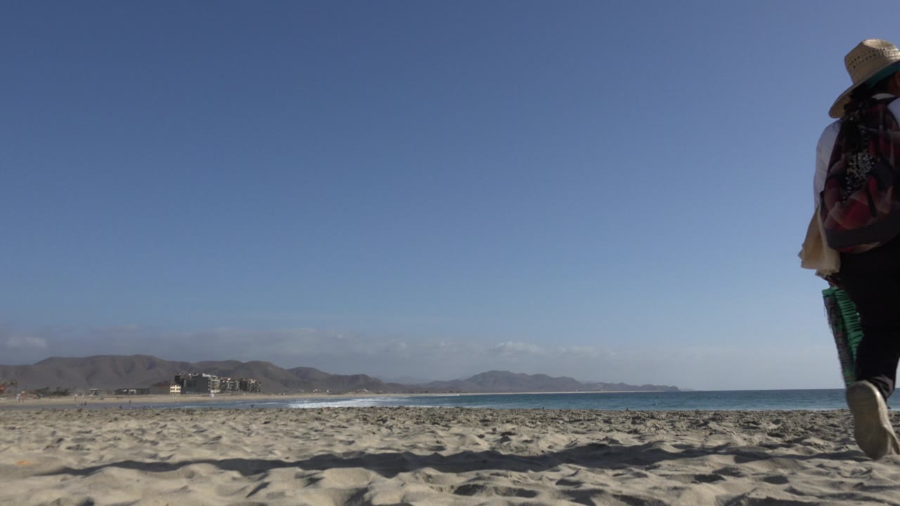 Person partly cropped walking on a sandy beach beside the sea.