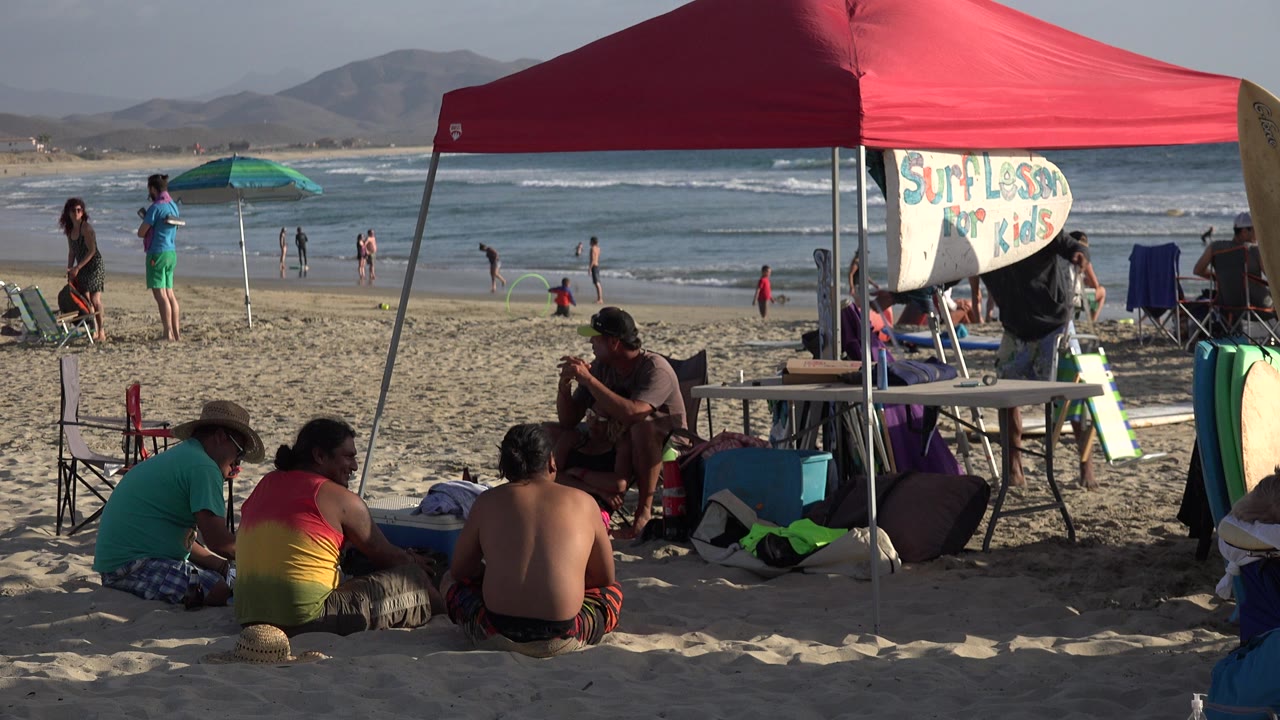 Beach surf lesson setup under a red canopy with people and waves behind it.