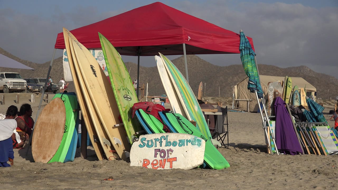 Surfboards and boogie boards for rent under a red beach canopy.