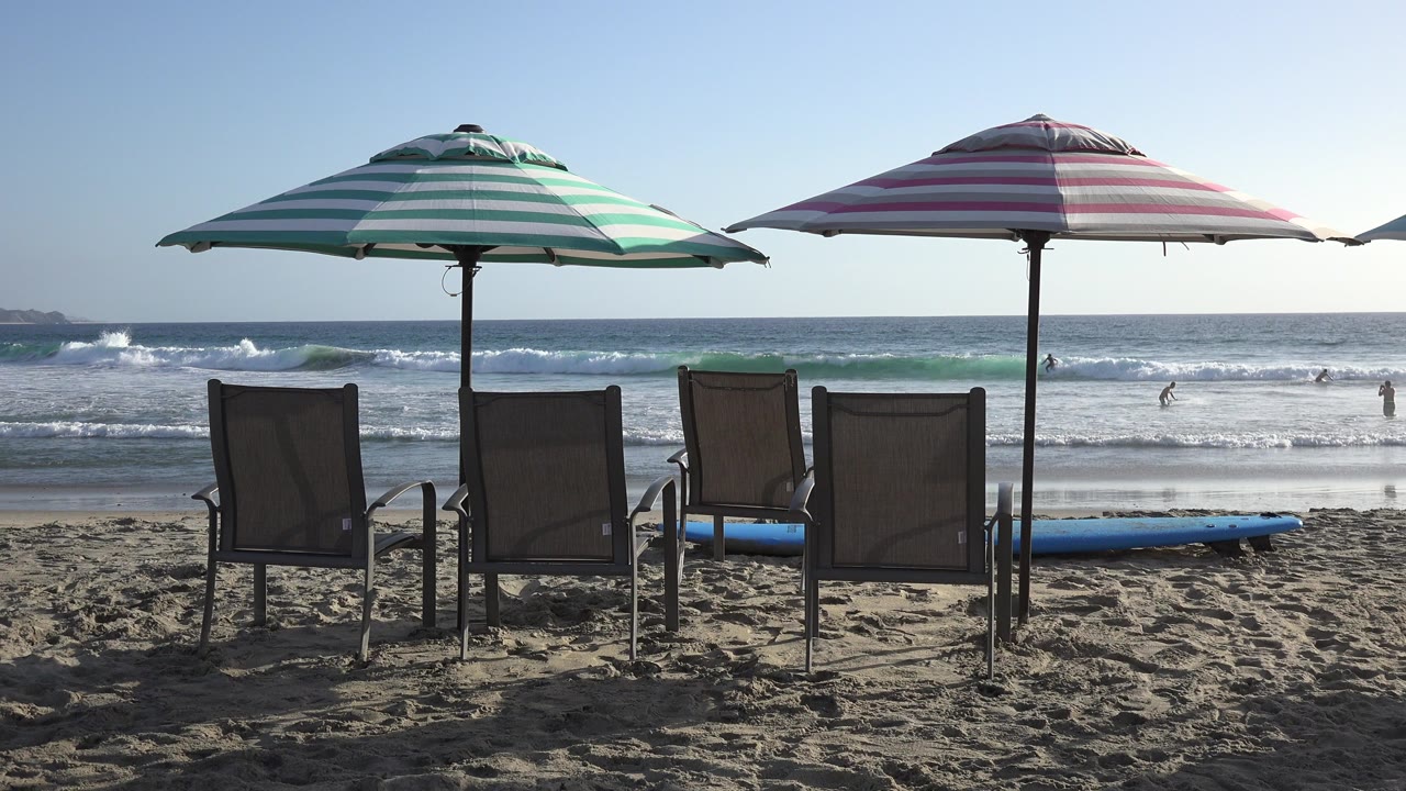Striped beach umbrellas over four chairs facing the ocean.