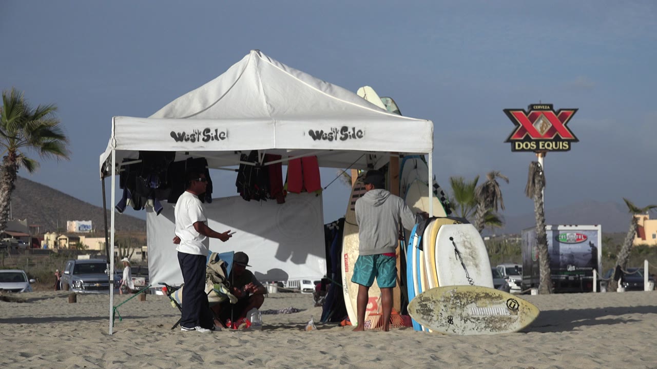 White beach pavilion with people and surfboards on sand.
