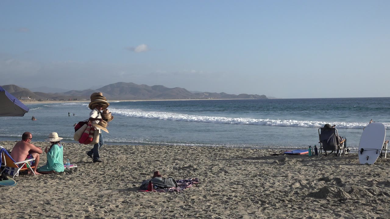 People relaxing on a beach with ocean waves and mountains beyond.