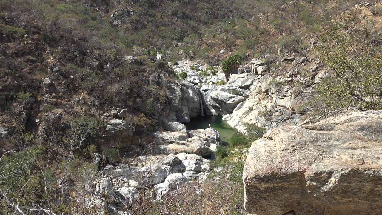 Rocky dry hillside with a dark cave opening and shrubs