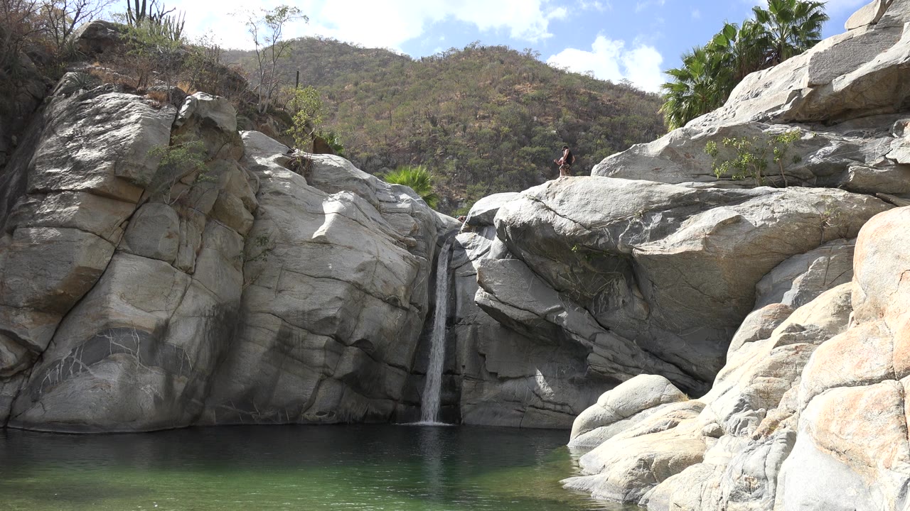 Small waterfall falling between large pale rocks into green water.