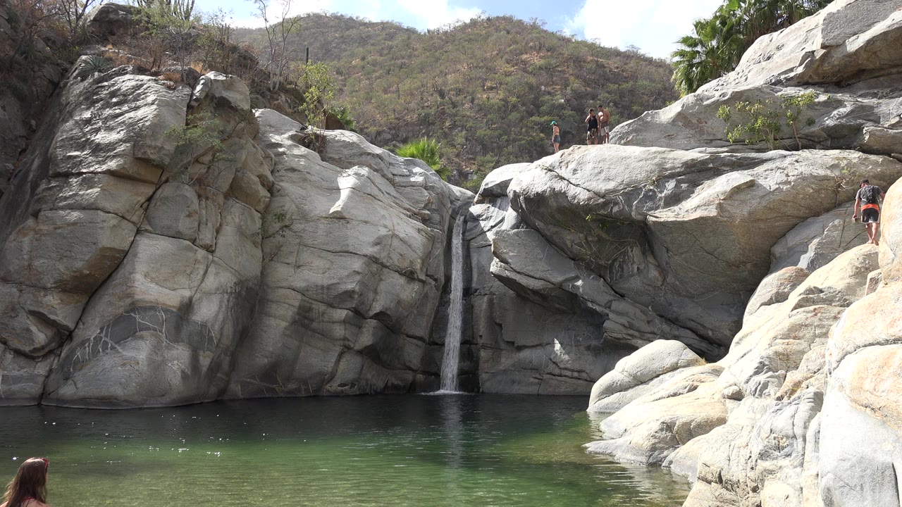 Rocky pool with small waterfall and people on ledges