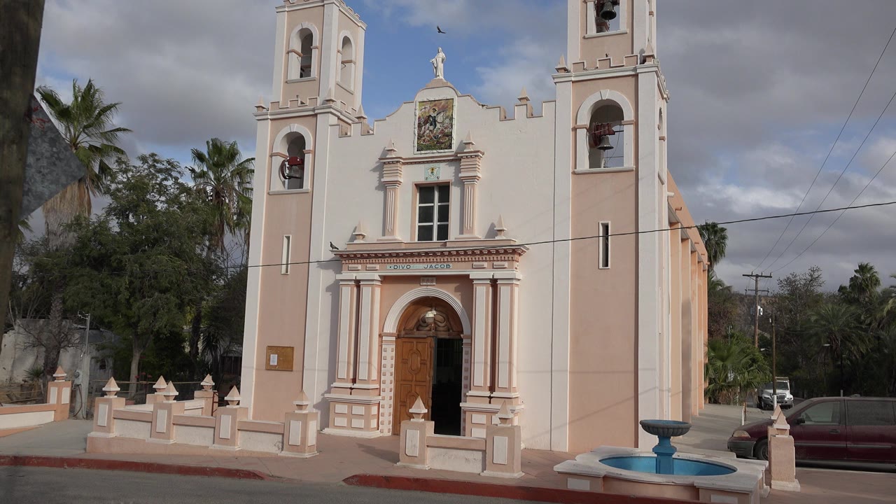 Pale church facade with bell towers and a fountain in front.